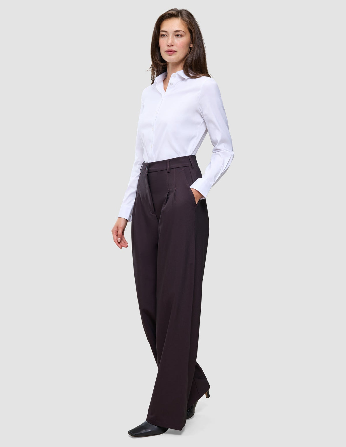 En kvinna bär en vit skjorta med knappar och dambyxorna Avira Pants Wide Burgundy Berry i en festlig passform.