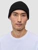 En man som bär en svart, ribbad mössa i merinoull, modell Beanie Black.