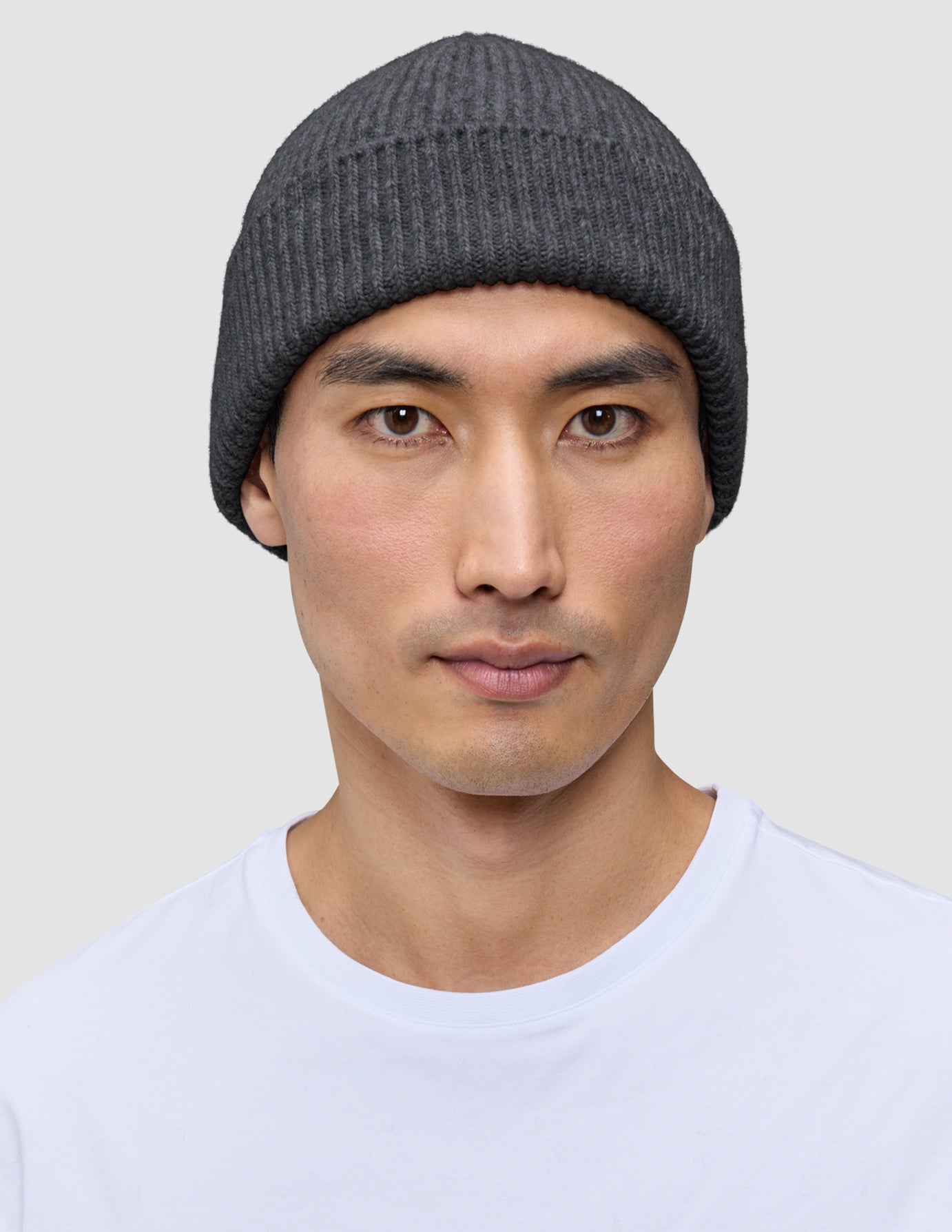 En person som bär en varm, mörkgrå, ribbad mössa i merinoull, modell Beanie Dark Grey.