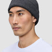 En person som bär en varm, mörkgrå, ribbad mössa i merinoull, modell Beanie Dark Grey.