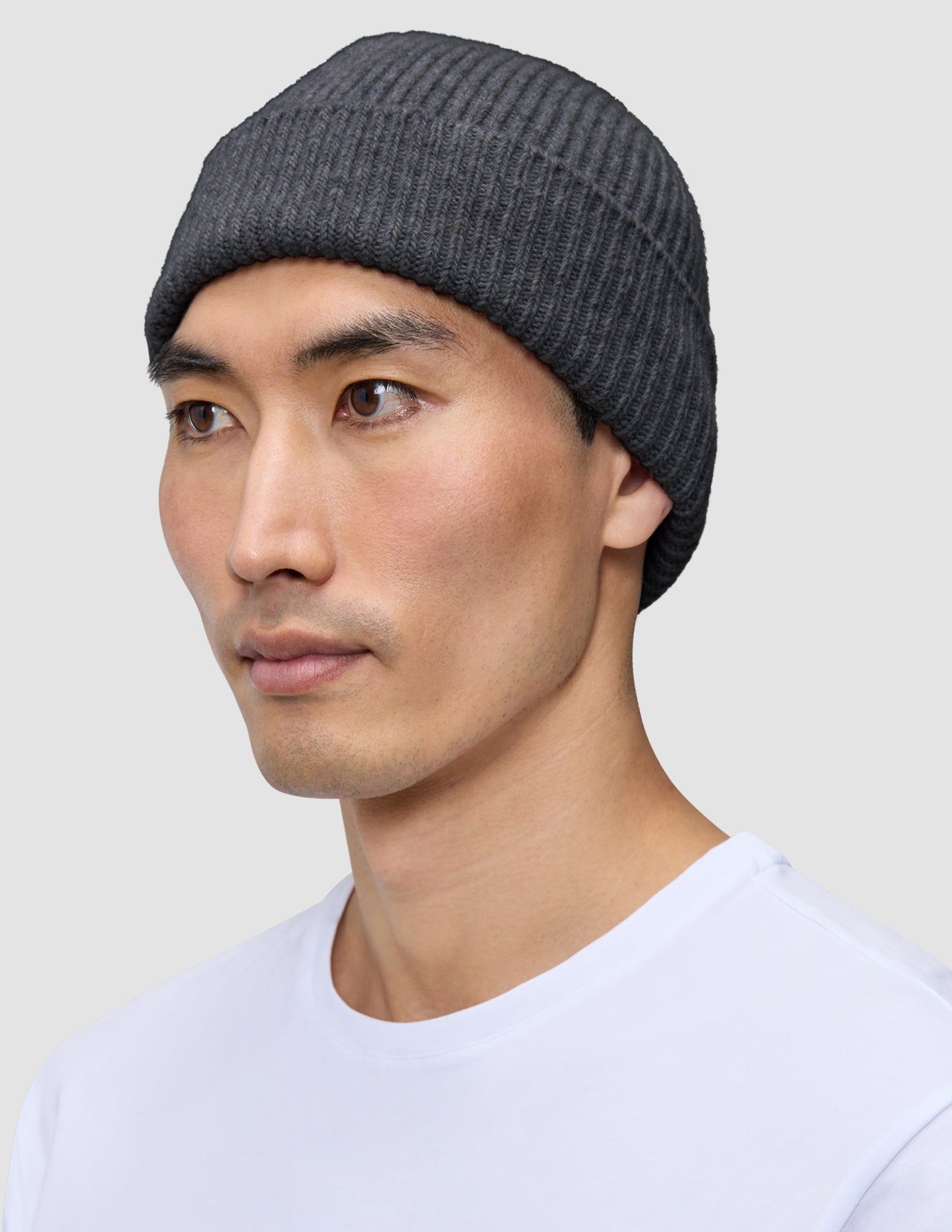 En person som bär en varm, mörkgrå, ribbad mössa i merinoull, modell Beanie Dark Grey.