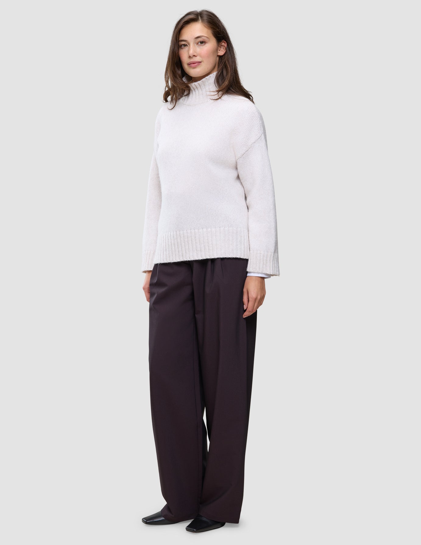 En kvinna klädd i en damtröja av typen Chunky Soft Wool Knit Turtleneck Sugar Melange och mörka byxor med vida ben.