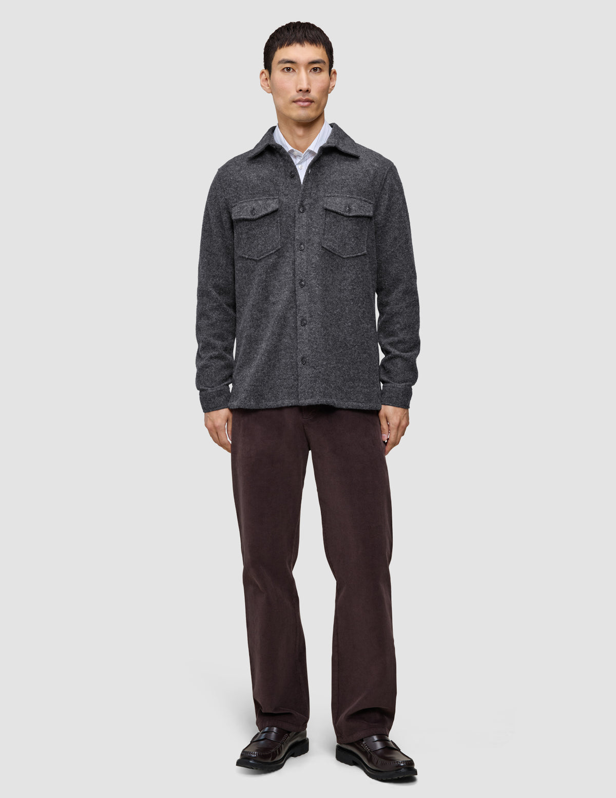 En man bär en dubbellagad yttertröja i ull, modell Regular, mörkgrå, över en vit skjorta, tillsammans med mörka byxor och loafers.