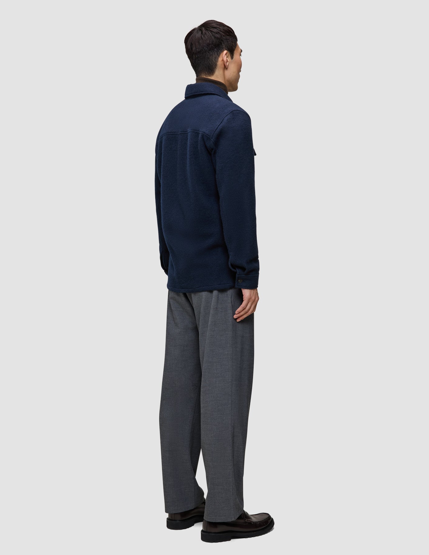 En person sedd bakifrån bär en dubbellagad ylleöverskjorta i mörk marinblått i regular-passform tillsammans med grå byxor i minimalistisk stil.