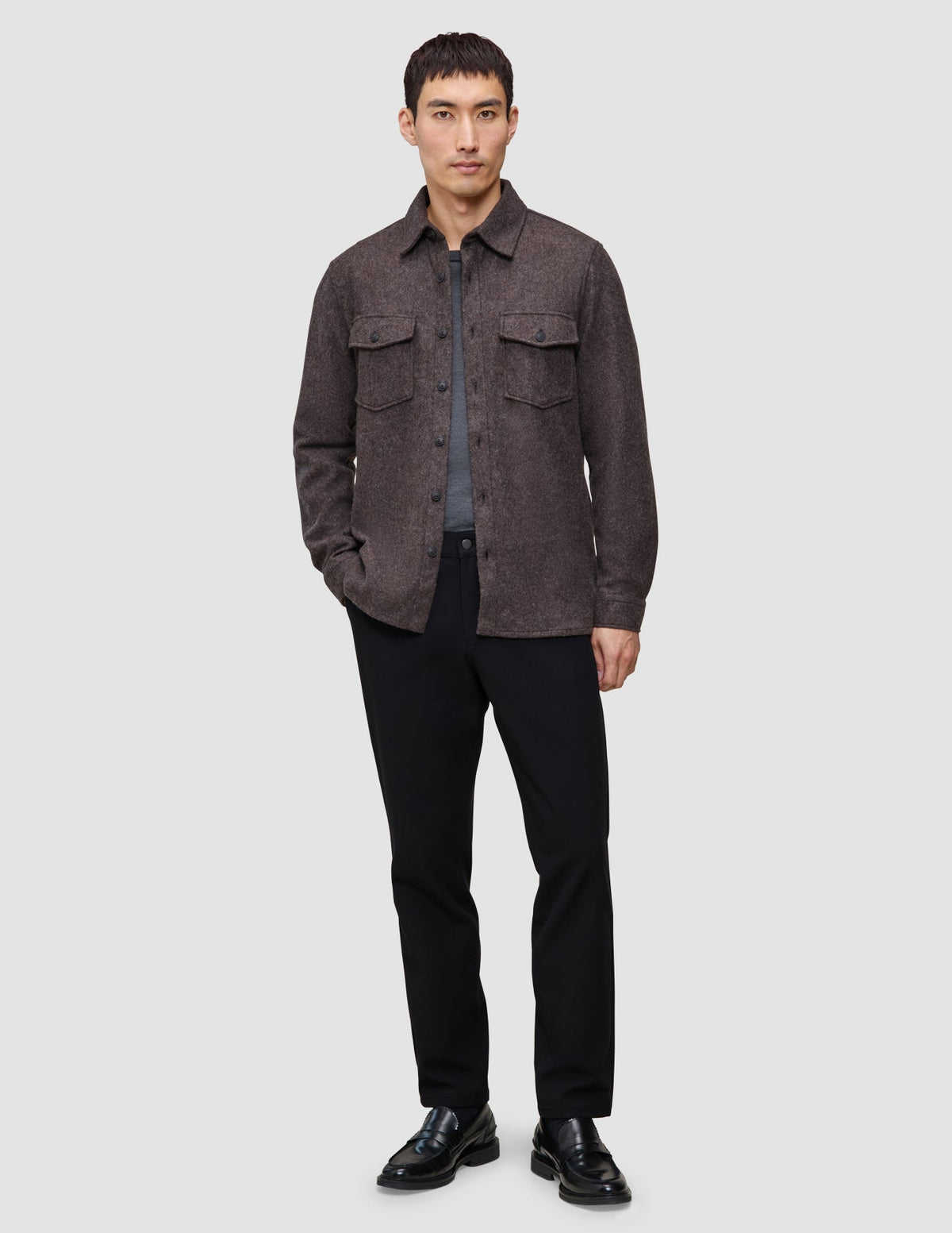 En man klädd i en dubbelskiktad ylleöverskjorta i sadelbrunt, en grå t-shirt, svarta byxor och svarta loafers.