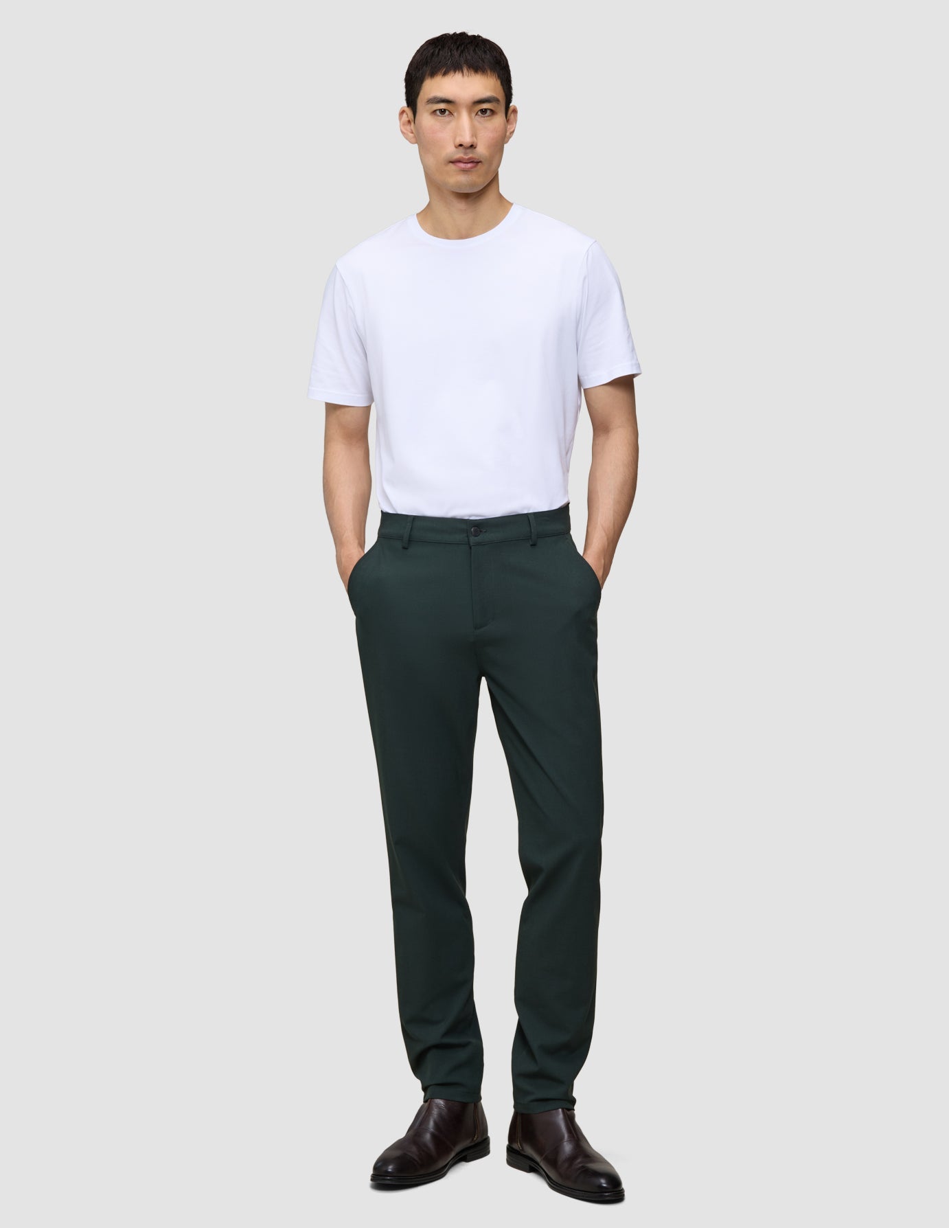 En man i en vit t-shirt och Ease Pants Regular Northern Pine med händerna i fickorna.