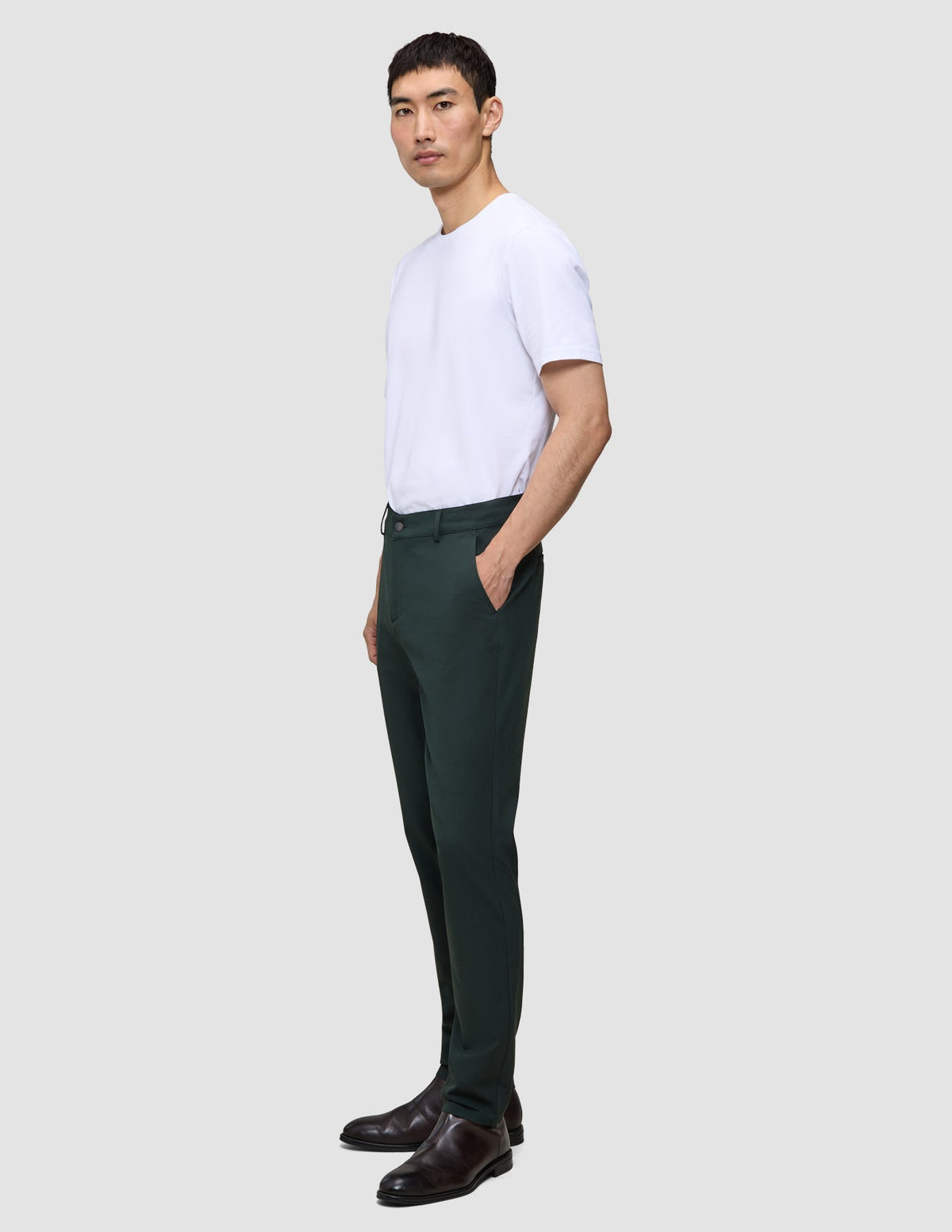 En man i en vit t-shirt och Ease Pants Regular Northern Pine står i profil och förkroppsligar den rena skandinaviska designen.