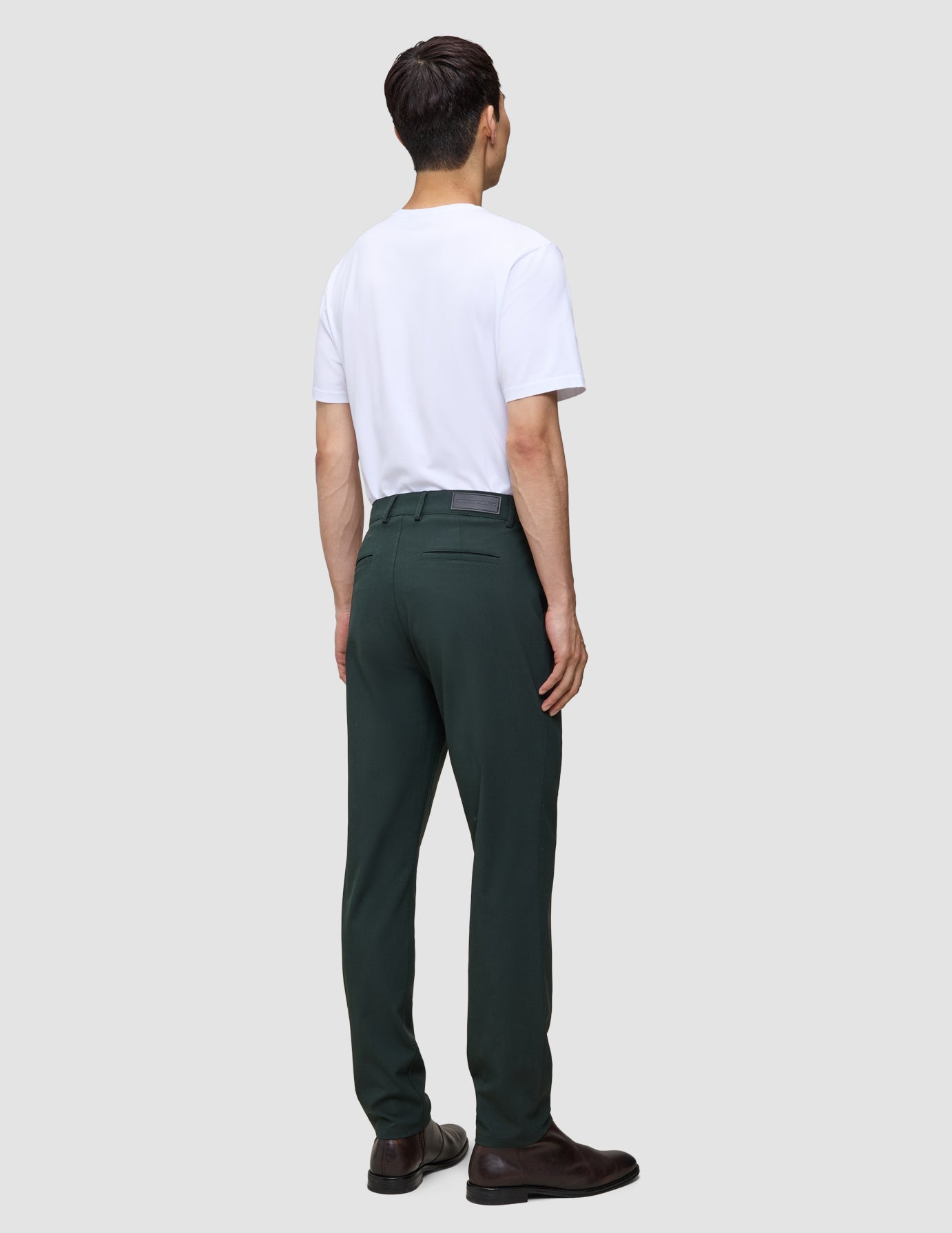 En person sedd bakifrån, klädd i en vit t-shirt, Ease Pants Regular Northern Pine och bruna kostymskor.