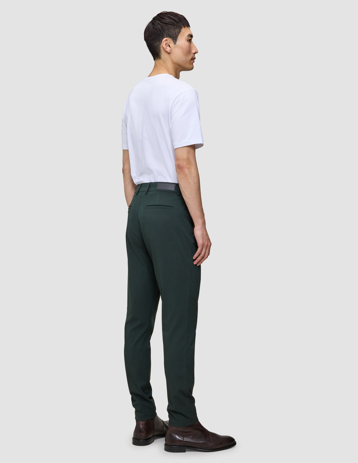 En person klädd i en vit t-shirt, Ease Pants Slim Northern Pine och bruna läderstövlar.