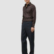 En man klädd i en mörkbrun skjorta av modellen Elevated Shirt Regular, kolgrå byxor och mörka loafers.