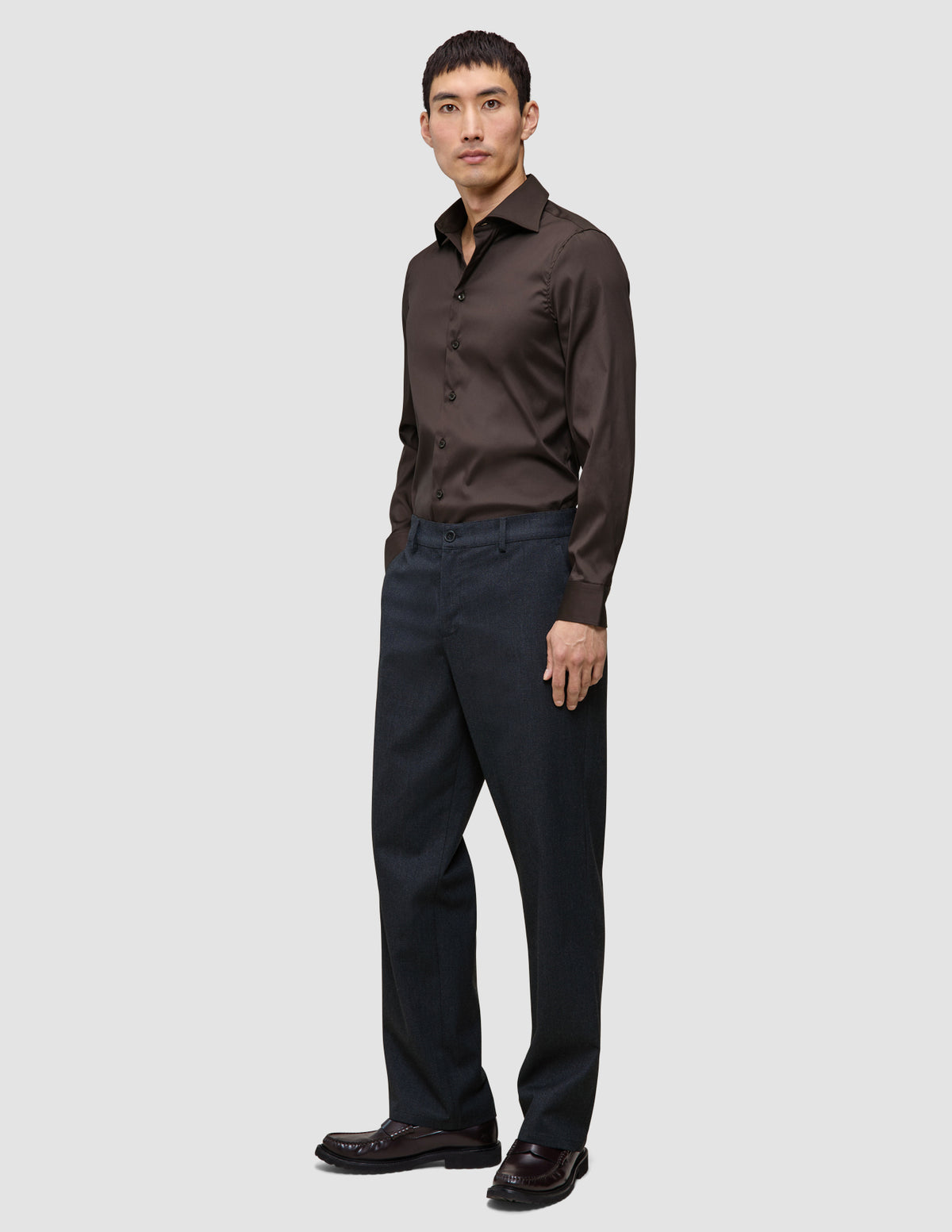 En man klädd i en mörkbrun skjorta av modellen Elevated Shirt Regular, kolgrå byxor och mörka loafers.