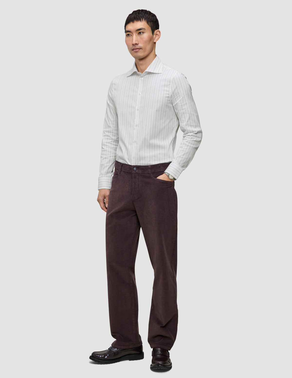 En man klädd i en ljusgrå randig skjorta av märket Elevated i modell Regular, mörka byxor och mörka loafers.
