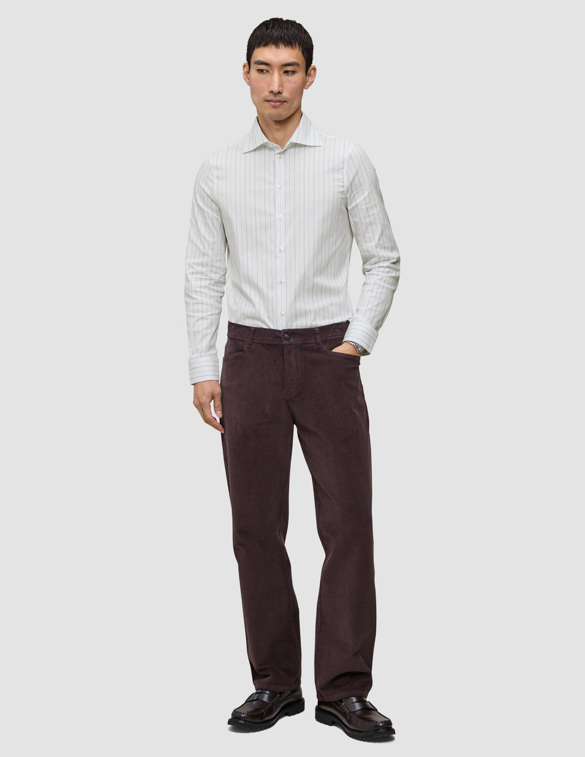 En man klädd i en ljusgrå randig skjorta av märket Elevated i modell Regular, mörka byxor och mörka loafers i skandinavisk design.