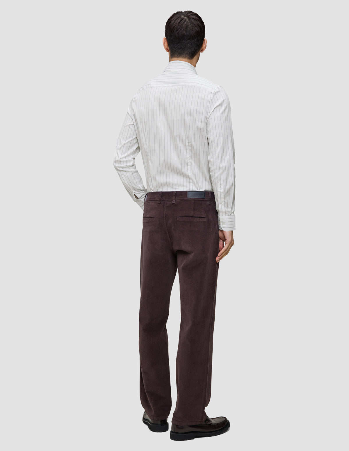 En man sedd bakifrån, klädd i en ljusgrå randig Elevated Shirt Regular som är instoppad i mörkbruna byxor och loafers.