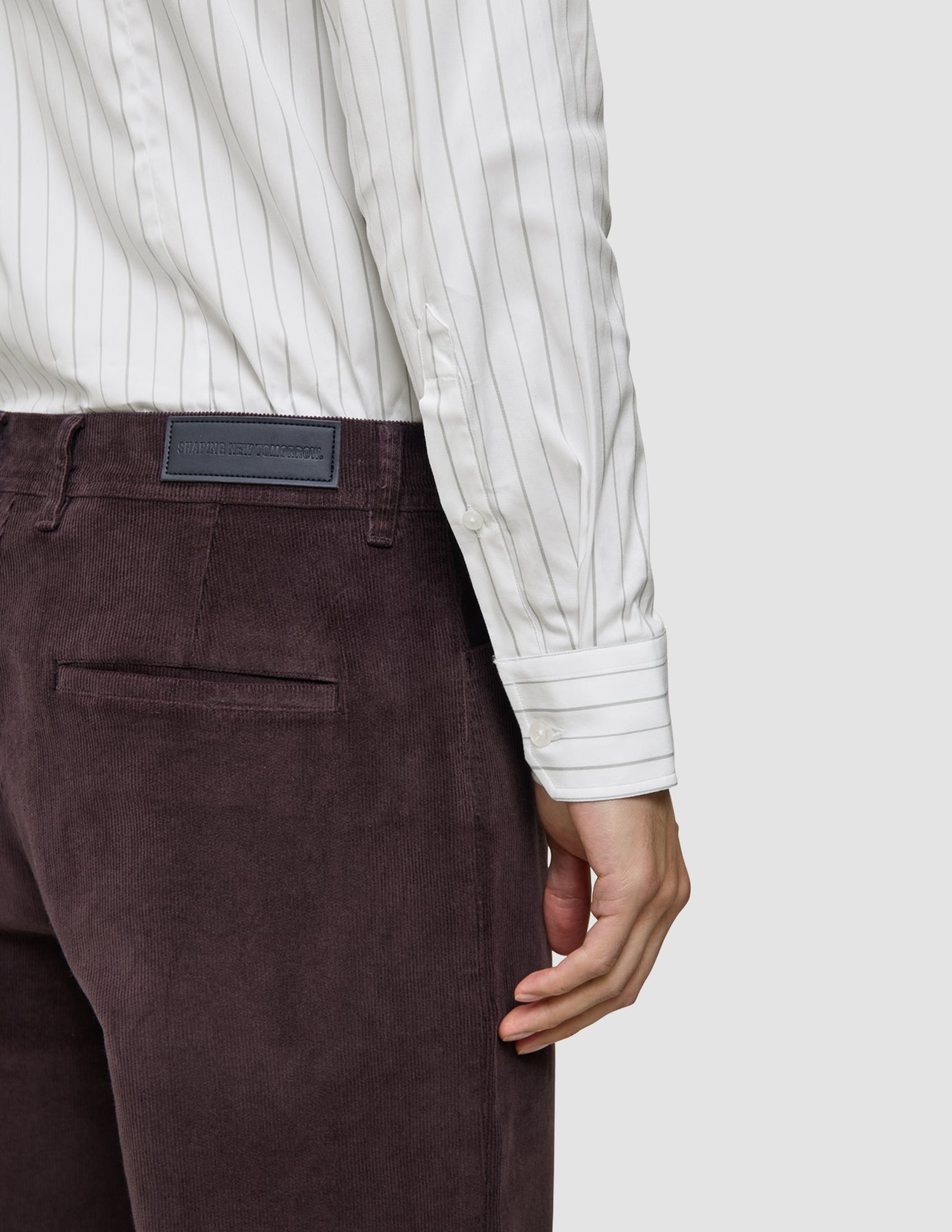 En person som bär en Elevated Shirt Regular i ljusgrå randigt och mörklila corduroybyxor.