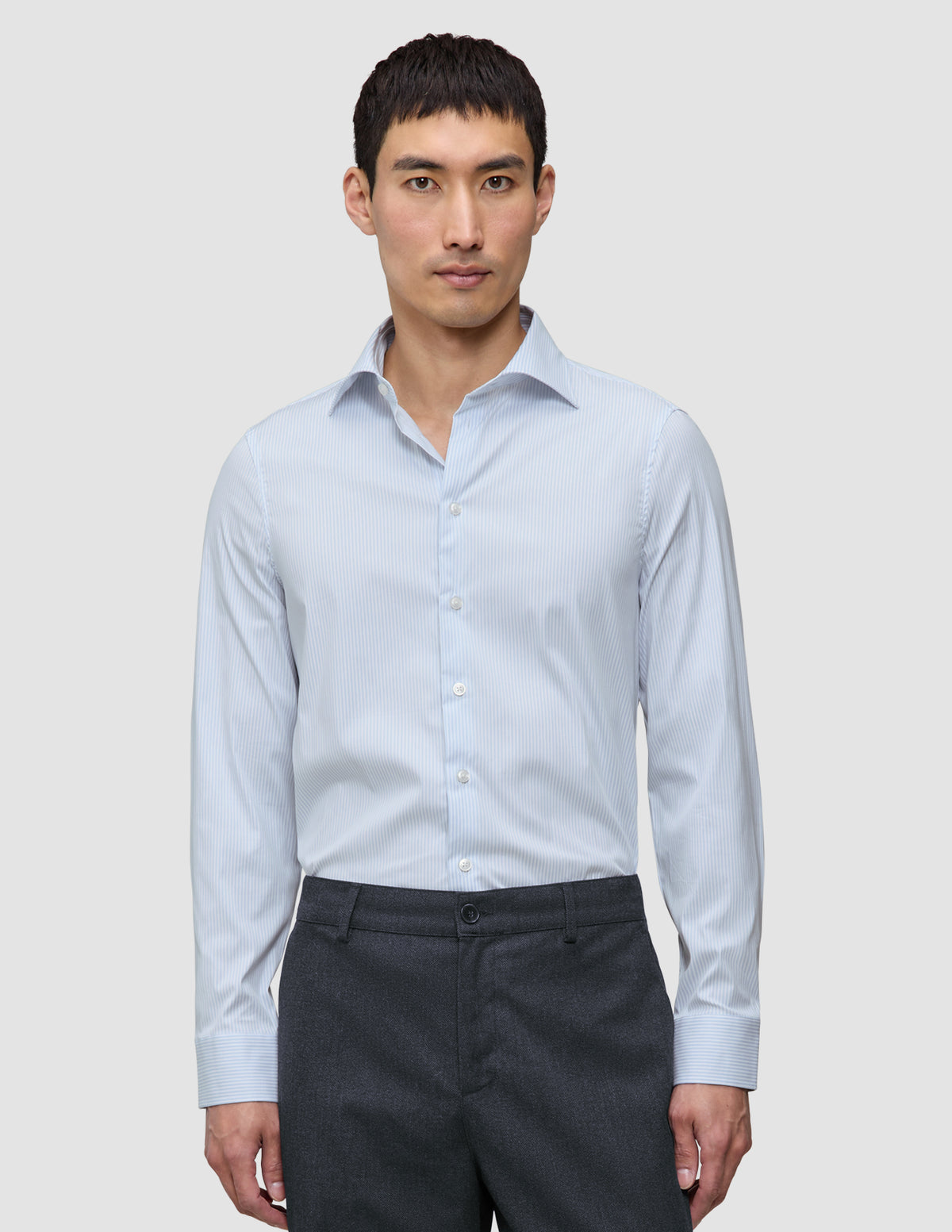 En man i en ljusblå och vitrandig Elevated Shirt Slim Classic Blue Striped tillsammans med mörkgrå byxor.