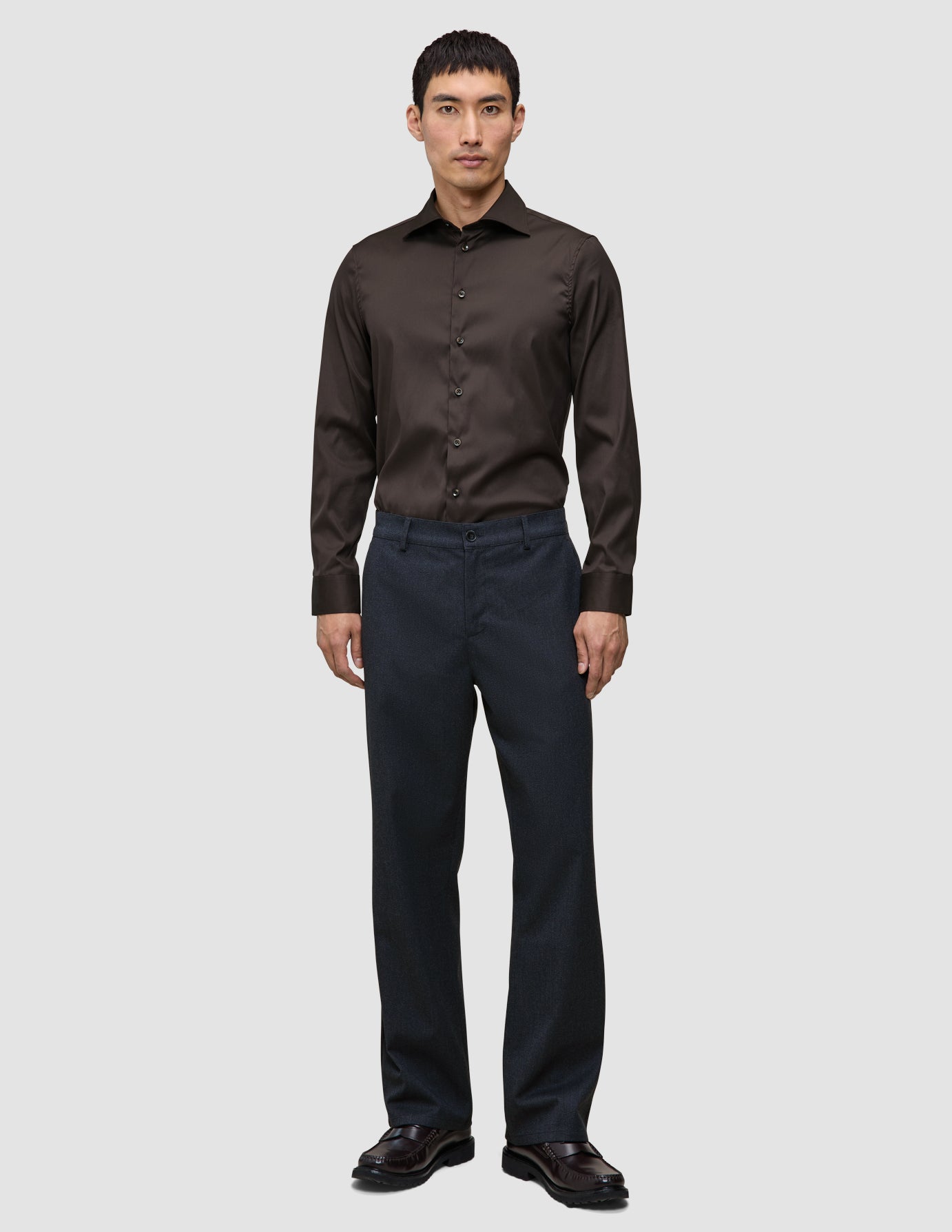 En man klädd i en mörkbrun Elevated Shirt Slim, instoppad i grå byxor och mörka läderskor.