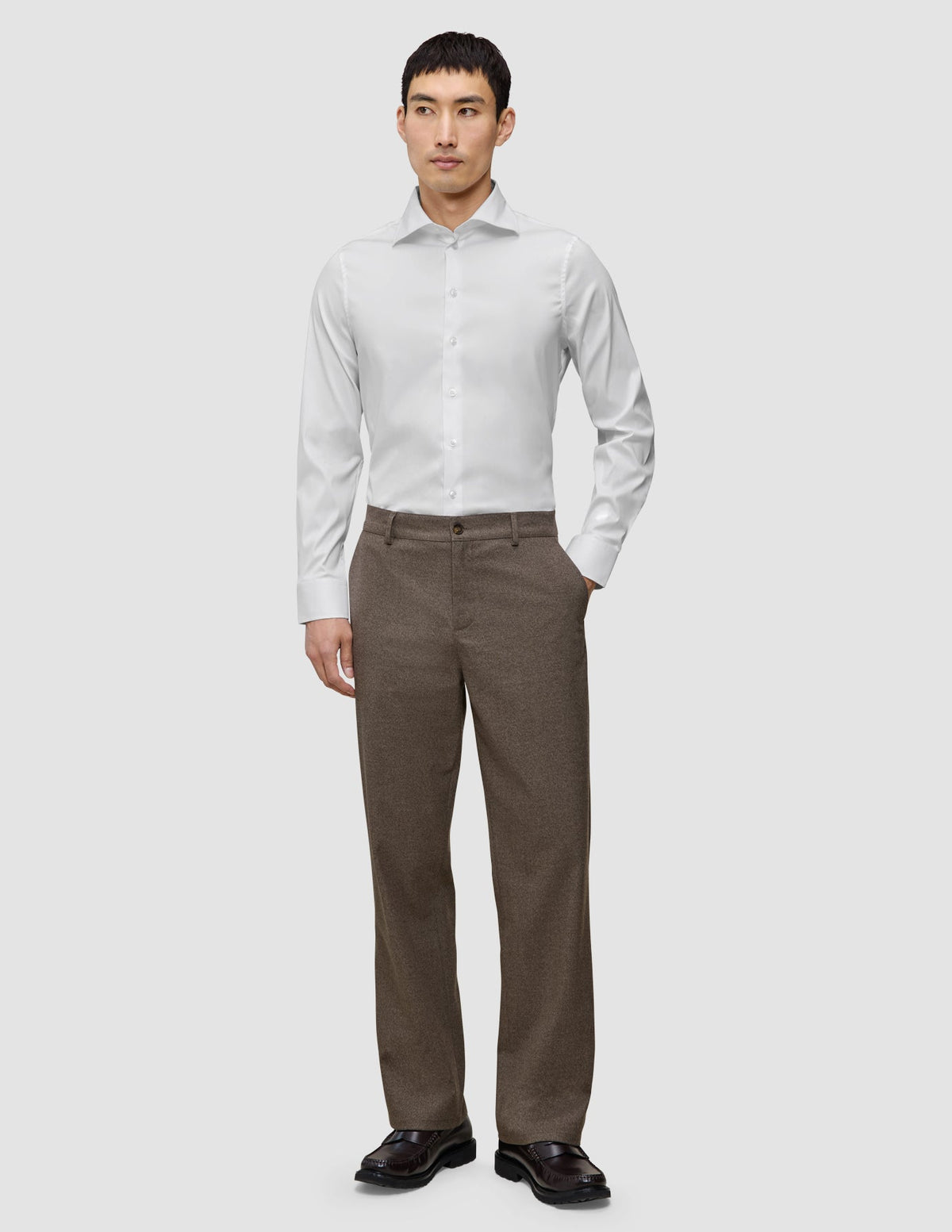 En man klädd i en vit, smal skjorta från Elevated, instoppad i bruna byxor och mörka loafers.