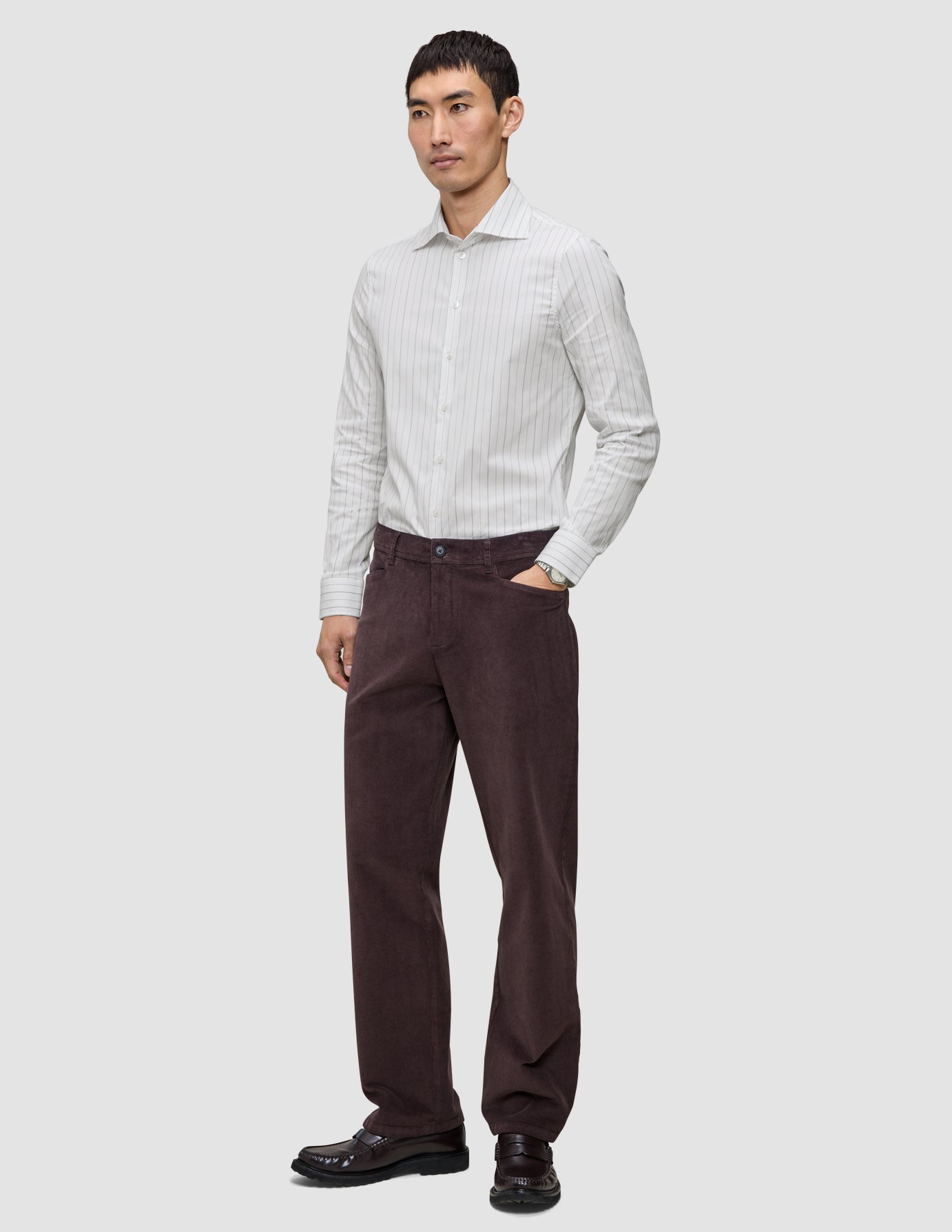En man bär en Elevated-skjorta i smal passform med ljusgrå ränder, instoppad i mörkbruna byxor och mörka loafers.
