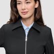 En person som bär en minimalistisk Essential Short Zip Jacket Black över en ljusblå skjorta med knappar.