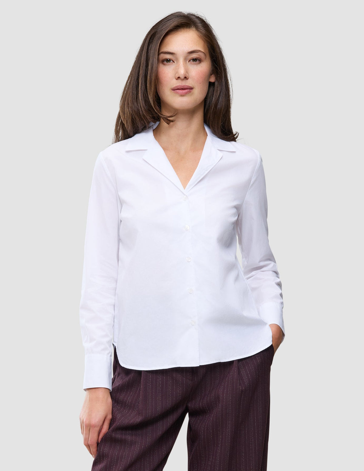 En kvinna klädd i en Madison Shirt White, en vit skjorta med knappar, skärad krage och långa ärmar.