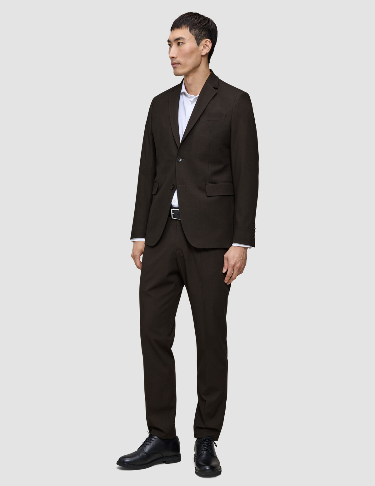 En man klädd i en Motion Blazer Regular Cognac, en vit skjorta och svarta läderskor.