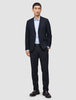 En man klädd i en blazer av modellen Motion Blazer Regular i färgen Midnight Blue och matchande byxor, en ljusblå skjorta och mörka loafers.