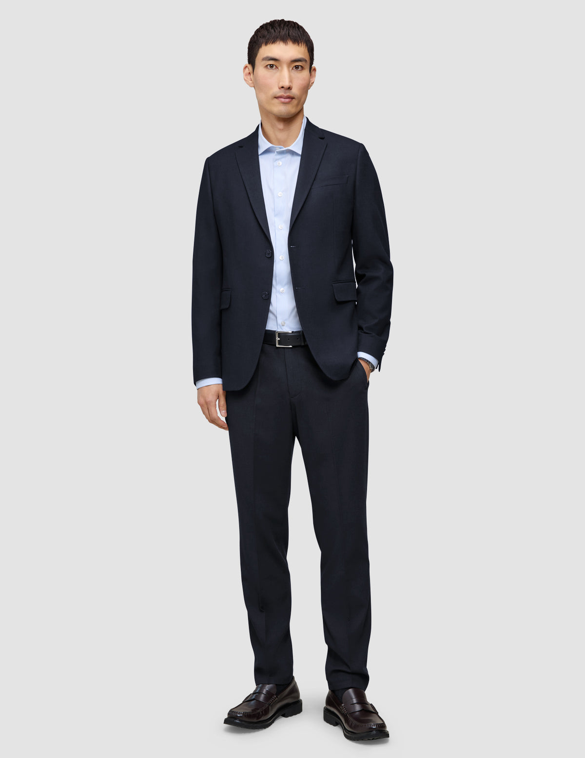 En man klädd i en blazer av modellen Motion Blazer Regular i färgen Midnight Blue och matchande byxor, en ljusblå skjorta och mörka loafers.