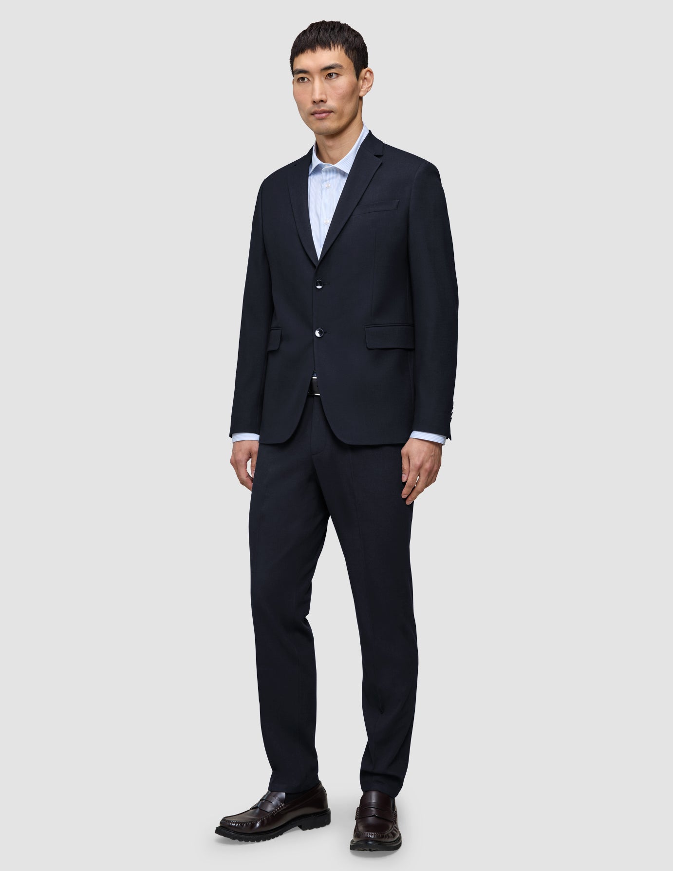 En man klädd i en kostym från Motion Blazer i storlek Regular i färgen Midnight Blue och matchande byxor, med en ljusblå skjorta och bruna loafers.