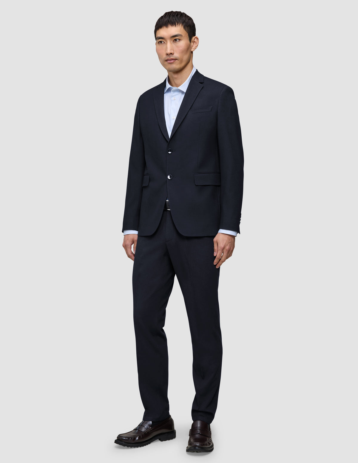 En man klädd i en kostym från Motion Blazer i storlek Regular i färgen Midnight Blue och matchande byxor, med en ljusblå skjorta och bruna loafers.