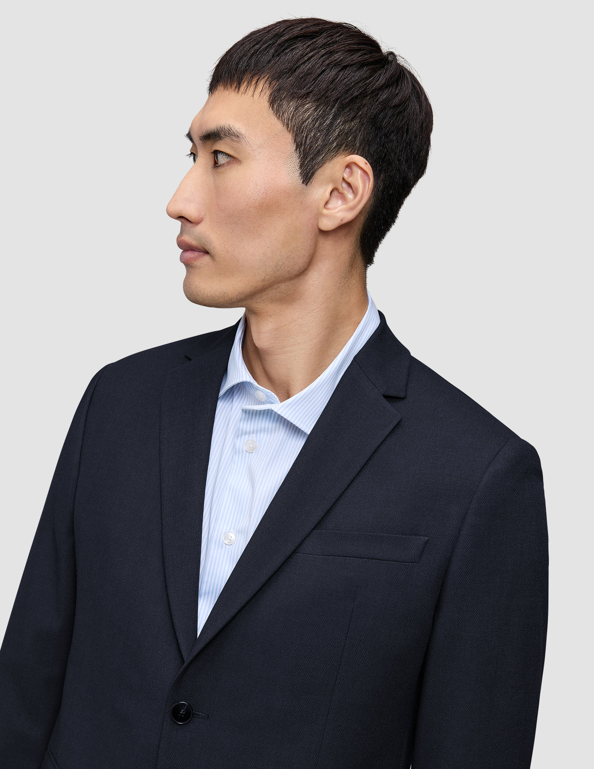 En man i en Motion Blazer Regular i färgen Midnight Blue, som han bär över en ljusblå randig skjorta med knappar.