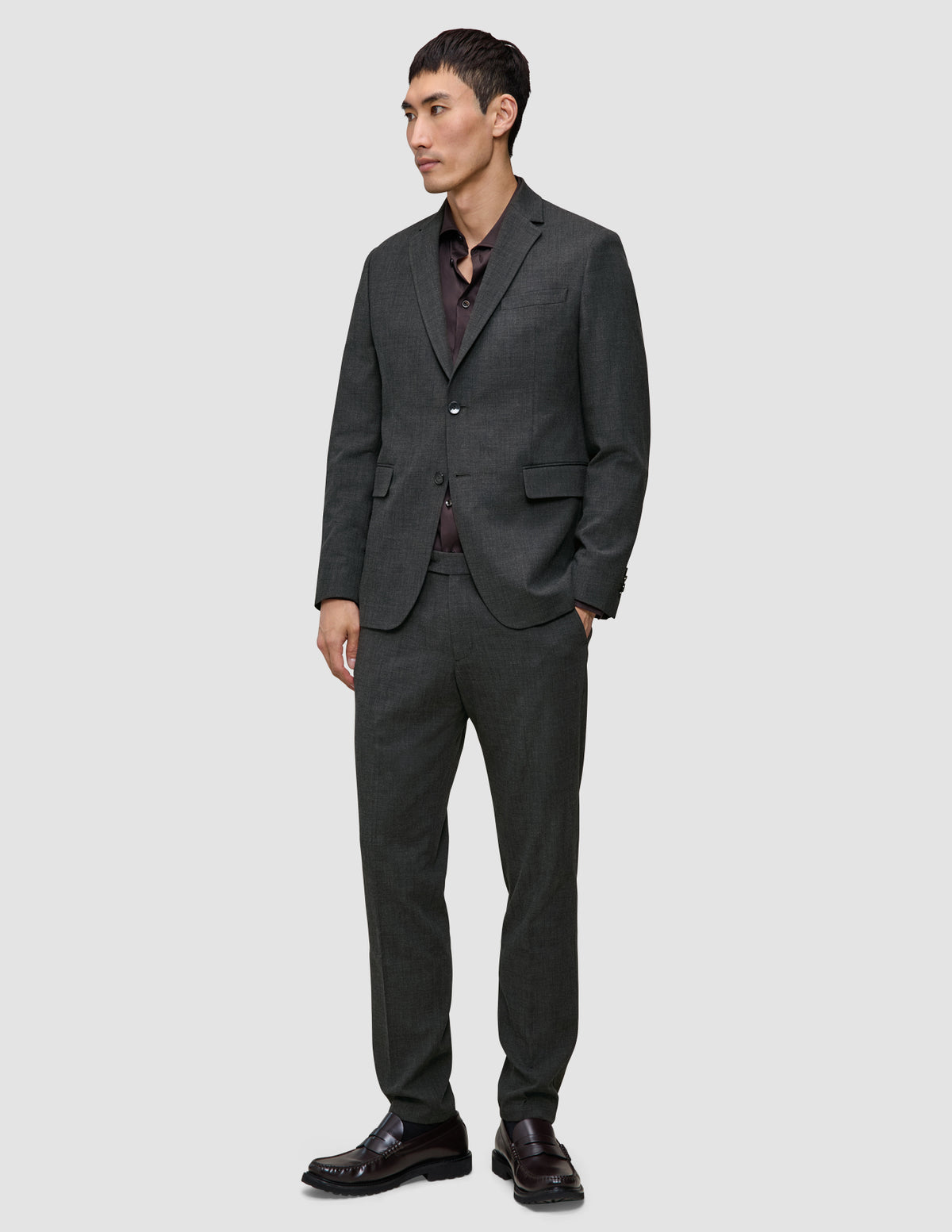 En man bär en Motion Blazer Regular i färgen Pepper Grey och matchande byxor över en mörk skjorta med knappar och loafers.