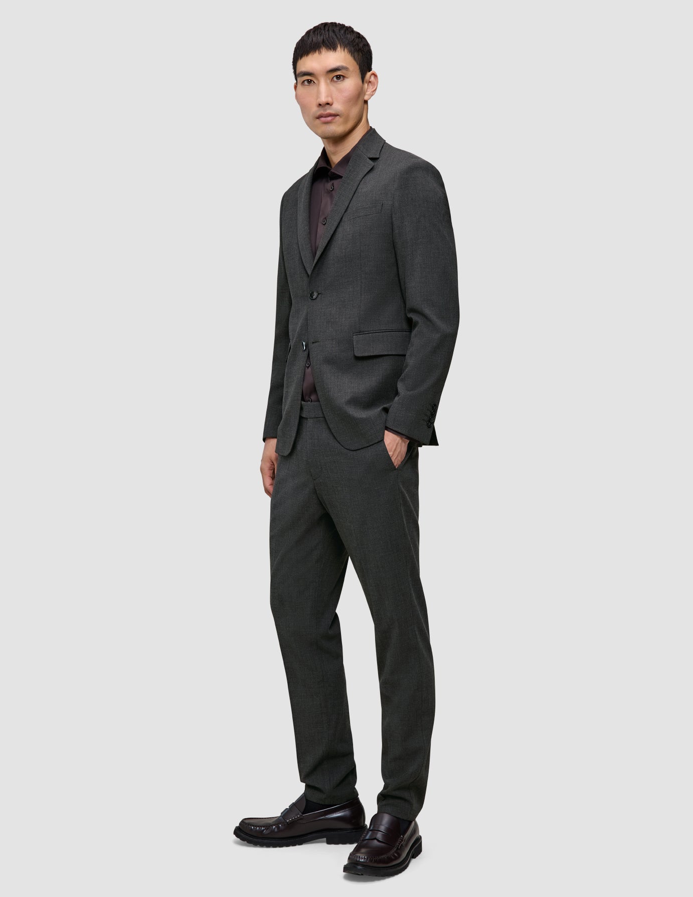 En man klädd i en Motion Blazer Regular i färgen Pepper Grey, en mörk skjorta med knappar, byxor och loafers, utformade för 360°-stretch.