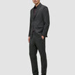 En man klädd i en Motion Blazer Regular i färgen Pepper Grey, en mörk skjorta med knappar, byxor och loafers, utformade för 360°-stretch.