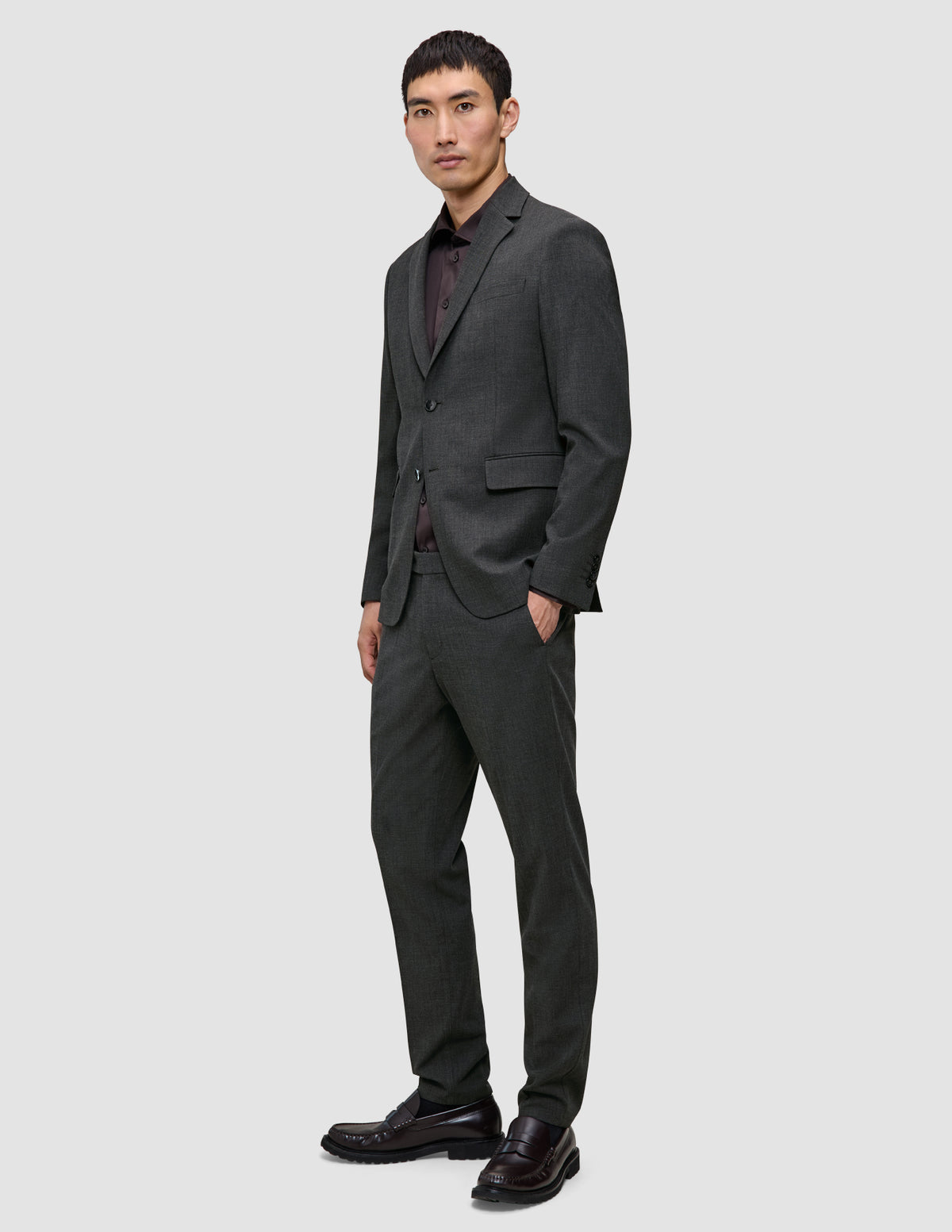 En man klädd i en Motion Blazer Regular i färgen Pepper Grey, en mörk skjorta med knappar, byxor och loafers, utformade för 360°-stretch.