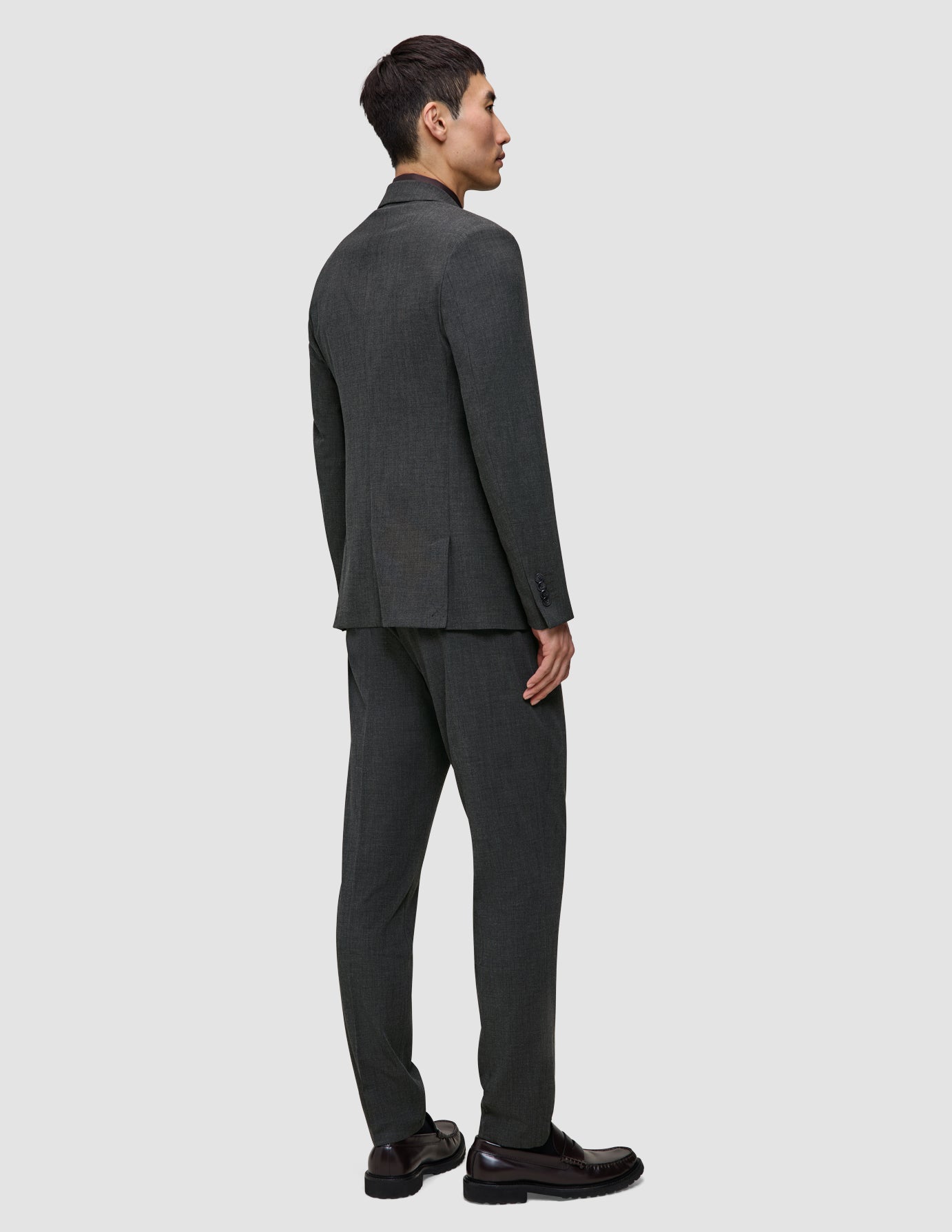 En man sedd bakifrån, klädd i en Motion Blazer Regular Pepper Grey-jacka och matchande byxor samt mörka loafers.