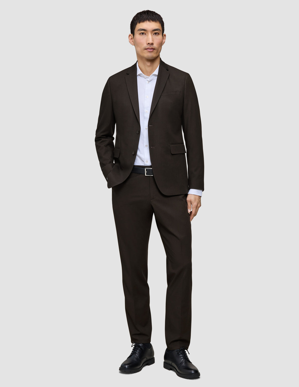 En man klädd i en Motion Blazer Slim Cognac och matchande byxor, vit skjorta, svart bälte och läderskor.