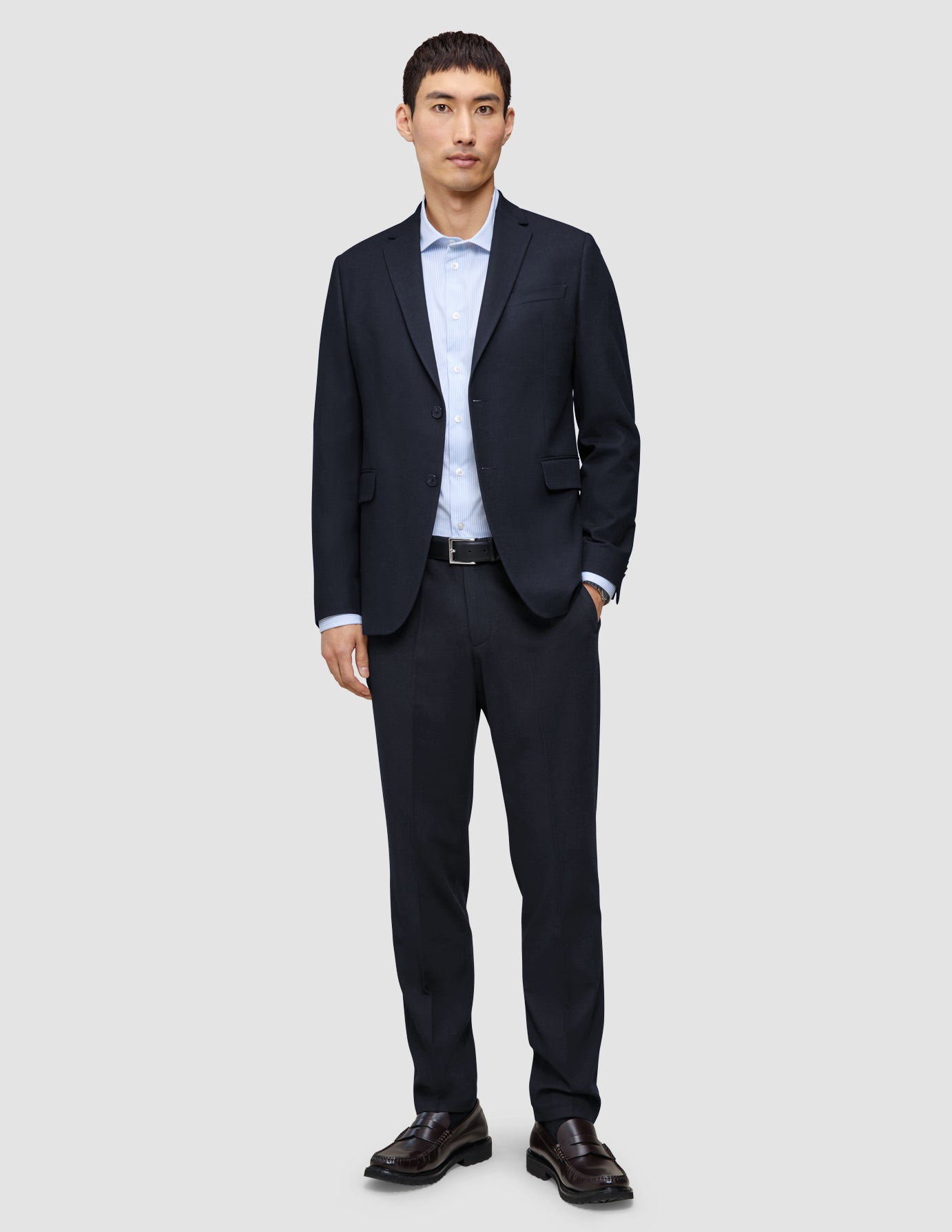 En man bär en Motion Blazer Slim i färgen Midnight Blue tillsammans med matchande byxor, en ljusblå skjorta och mörka loafers.