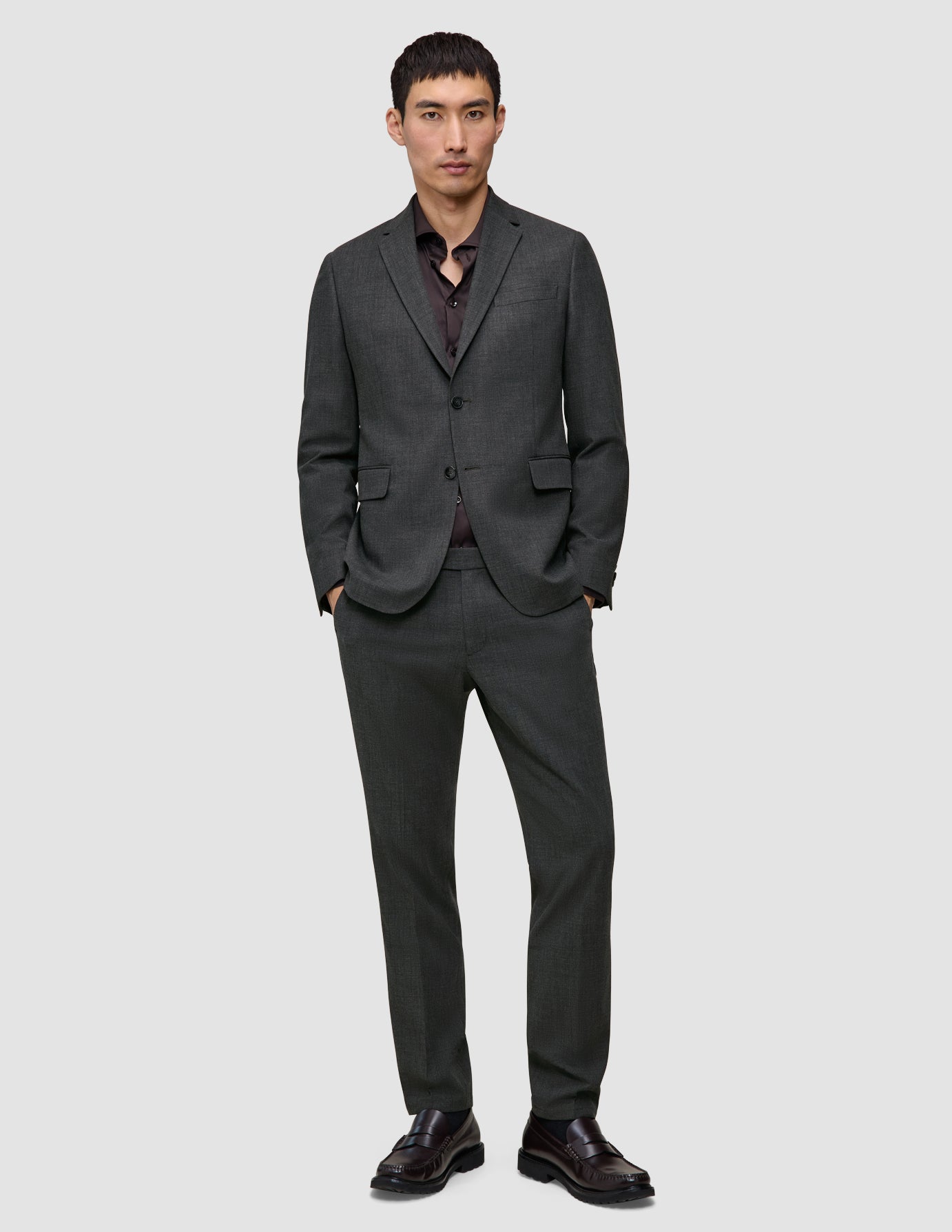 En man klädd i en Motion Blazer Slim i färgen Pepper Grey och en vinröd skjorta med knappar står med händerna i fickorna.