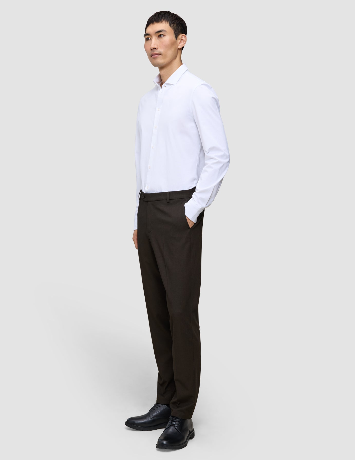 En man klädd i en vit skjorta med knappar och byxor av modellen Motion Suit Pants Regular Cognac med 360°-stretch.