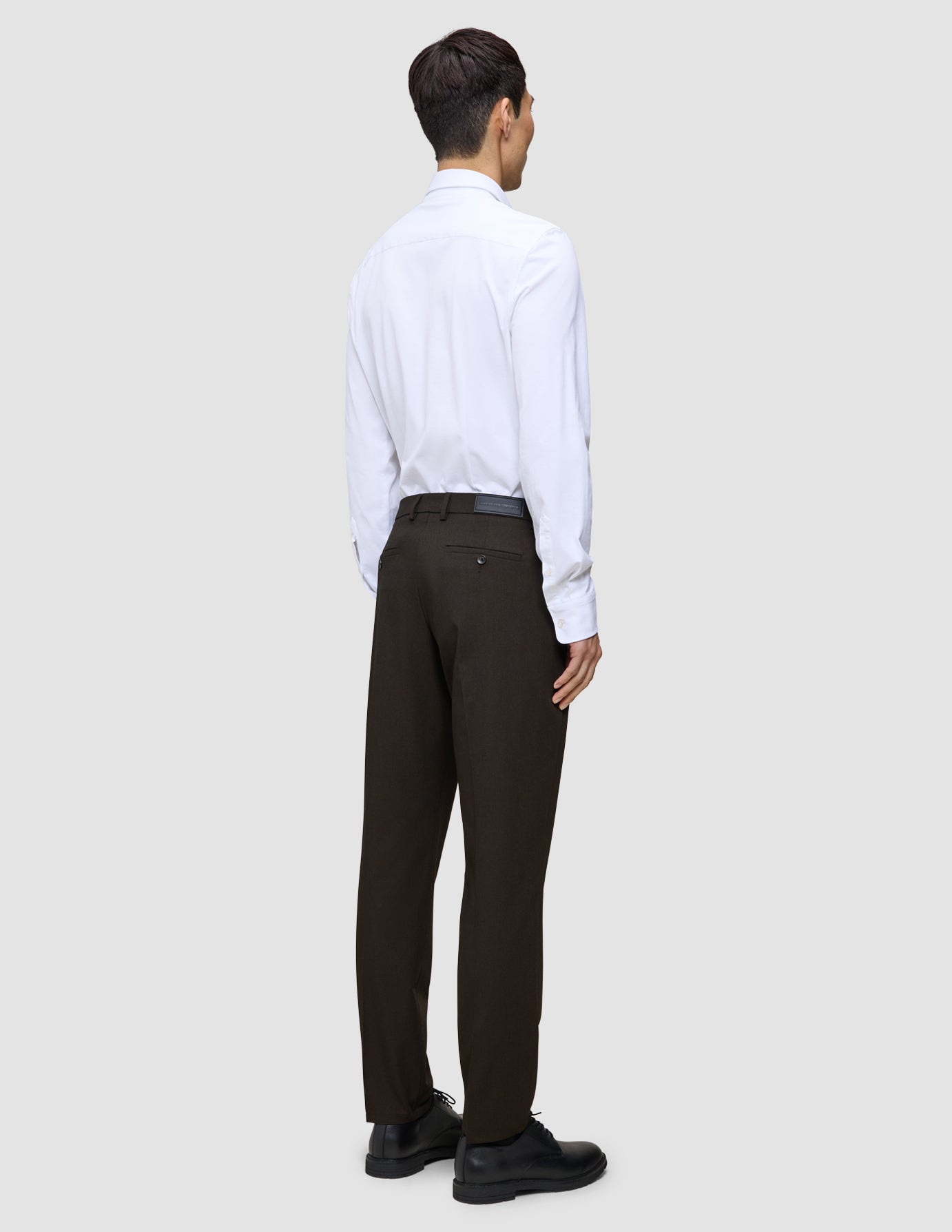 En person sedd bakifrån, klädd i en vit skjorta, byxor av modellen Motion Suit Pants Regular Cognac och svarta kostymskor.