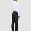 En person sedd bakifrån, klädd i en vit skjorta, byxor av modellen Motion Suit Pants Regular Cognac och svarta kostymskor.