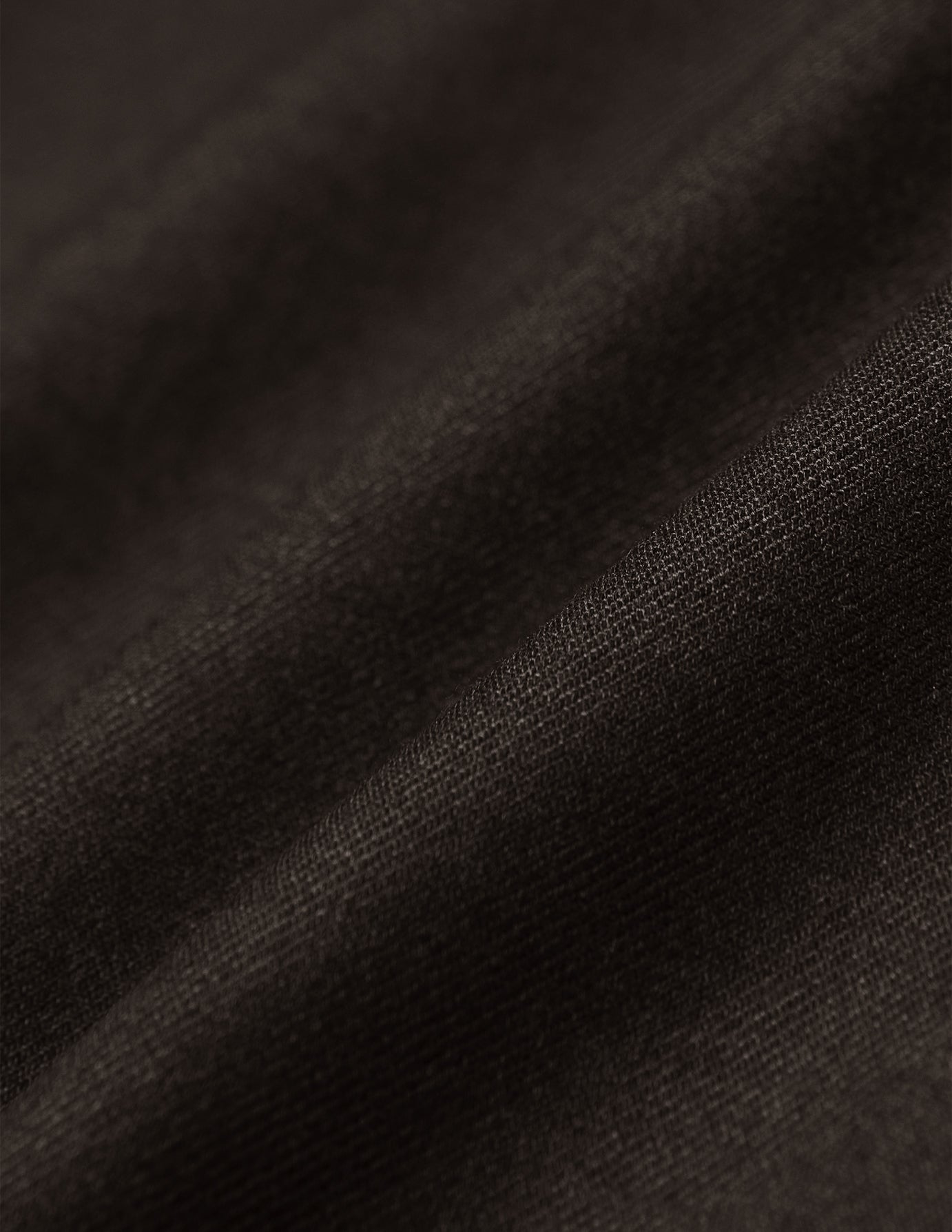Närbild på de mjuka veckningarna i det mörkbruna tyget på Motion Suit Pants Regular Cognac med 360°-stretch.
