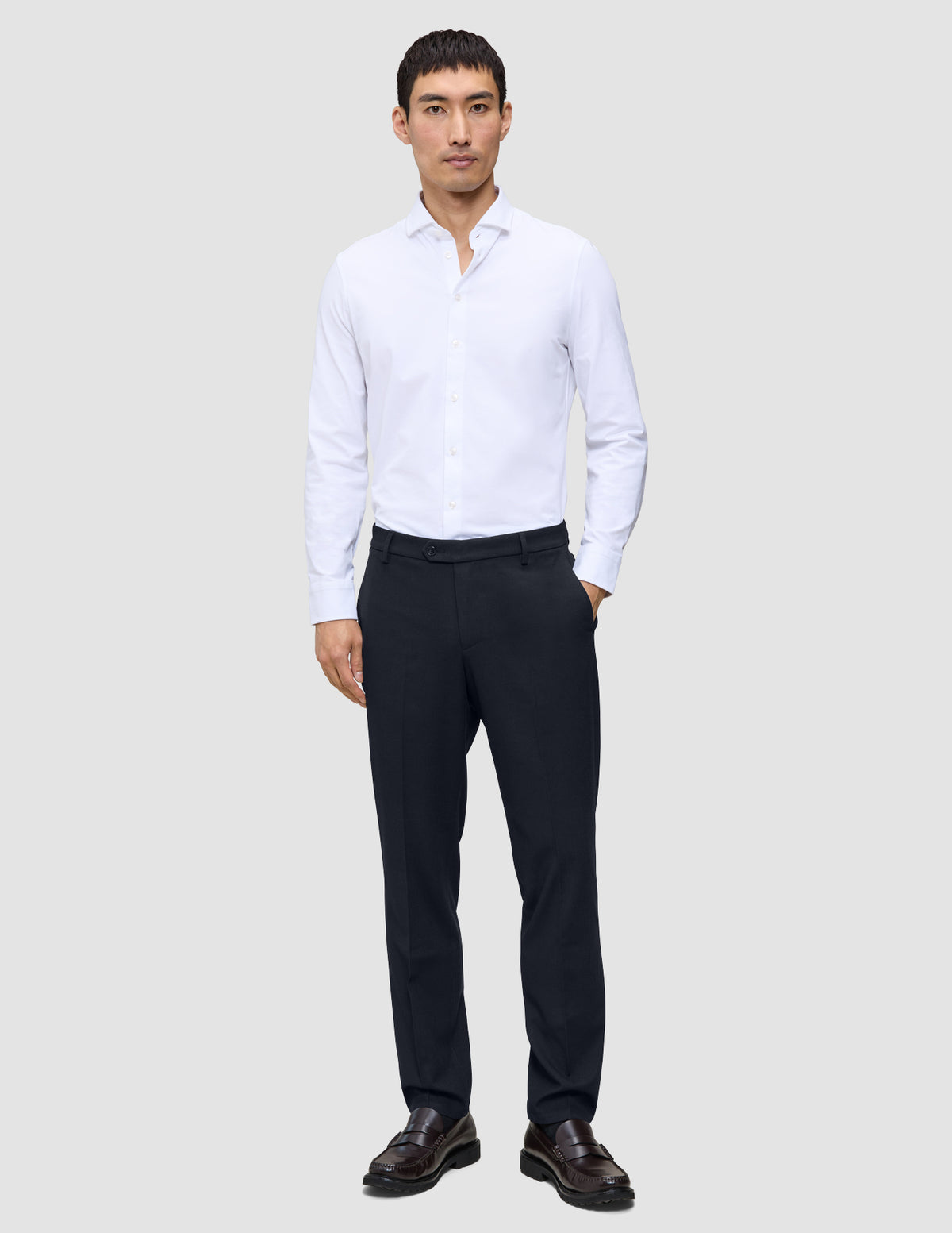 En man klädd i en vit skjorta, byxor av modellen Motion Suit Pants Regular i midnattsblått och bruna läderskor.