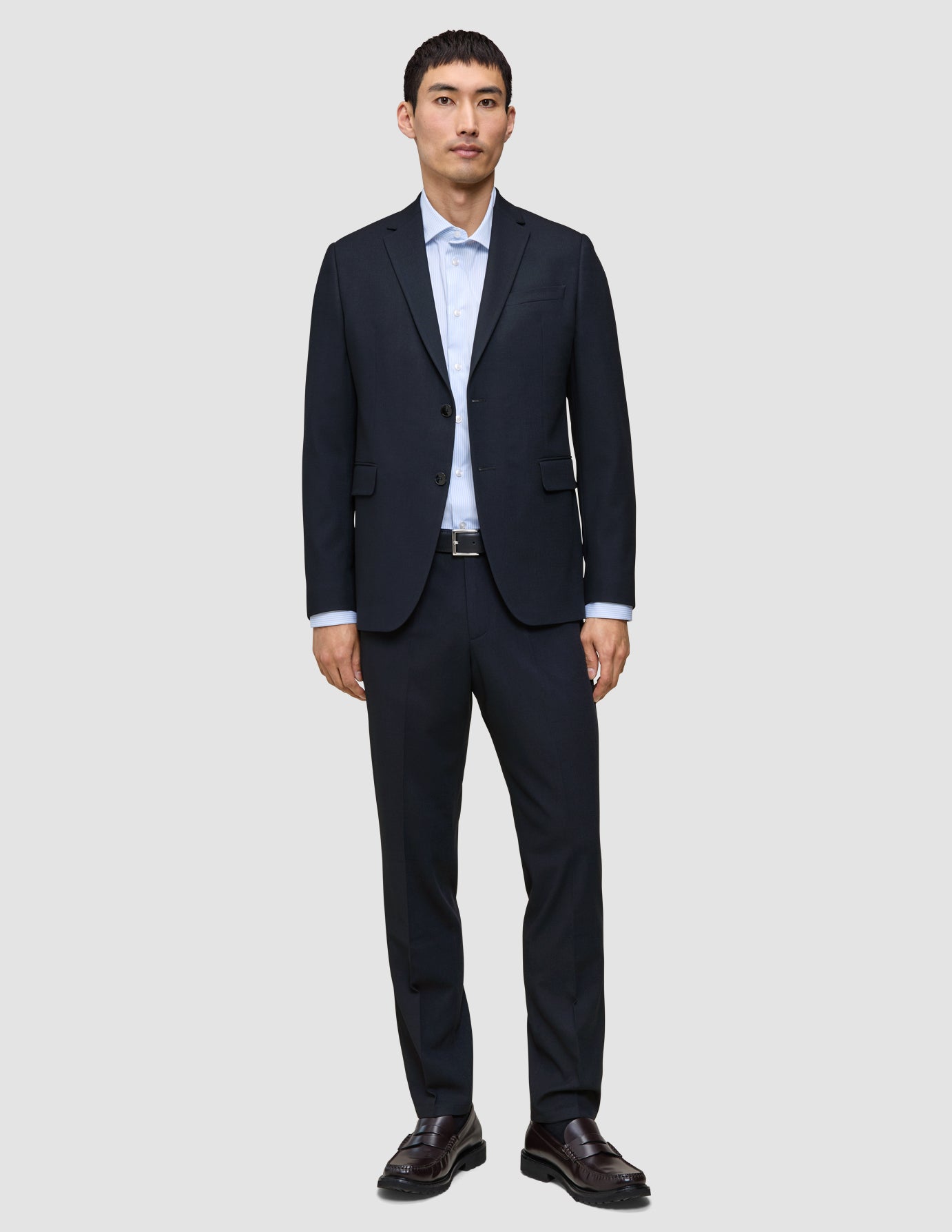 En man klädd i Motion Suit-byxor i storlek Regular i färgen Midnight Blue, en ljusblå skjorta och mörka läderskor.