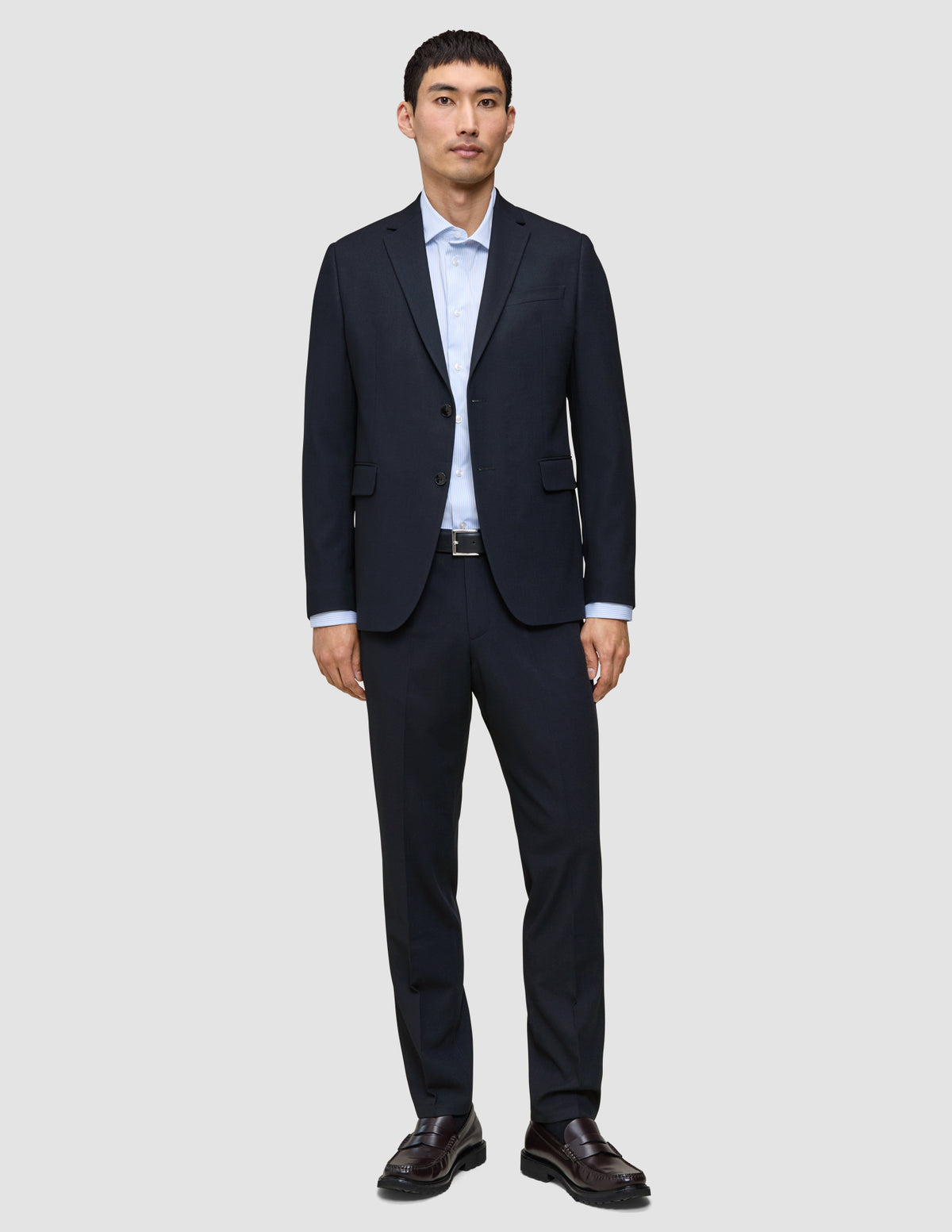 En man klädd i Motion Suit-byxor i storlek Regular i färgen Midnight Blue, en ljusblå skjorta och mörka läderskor.