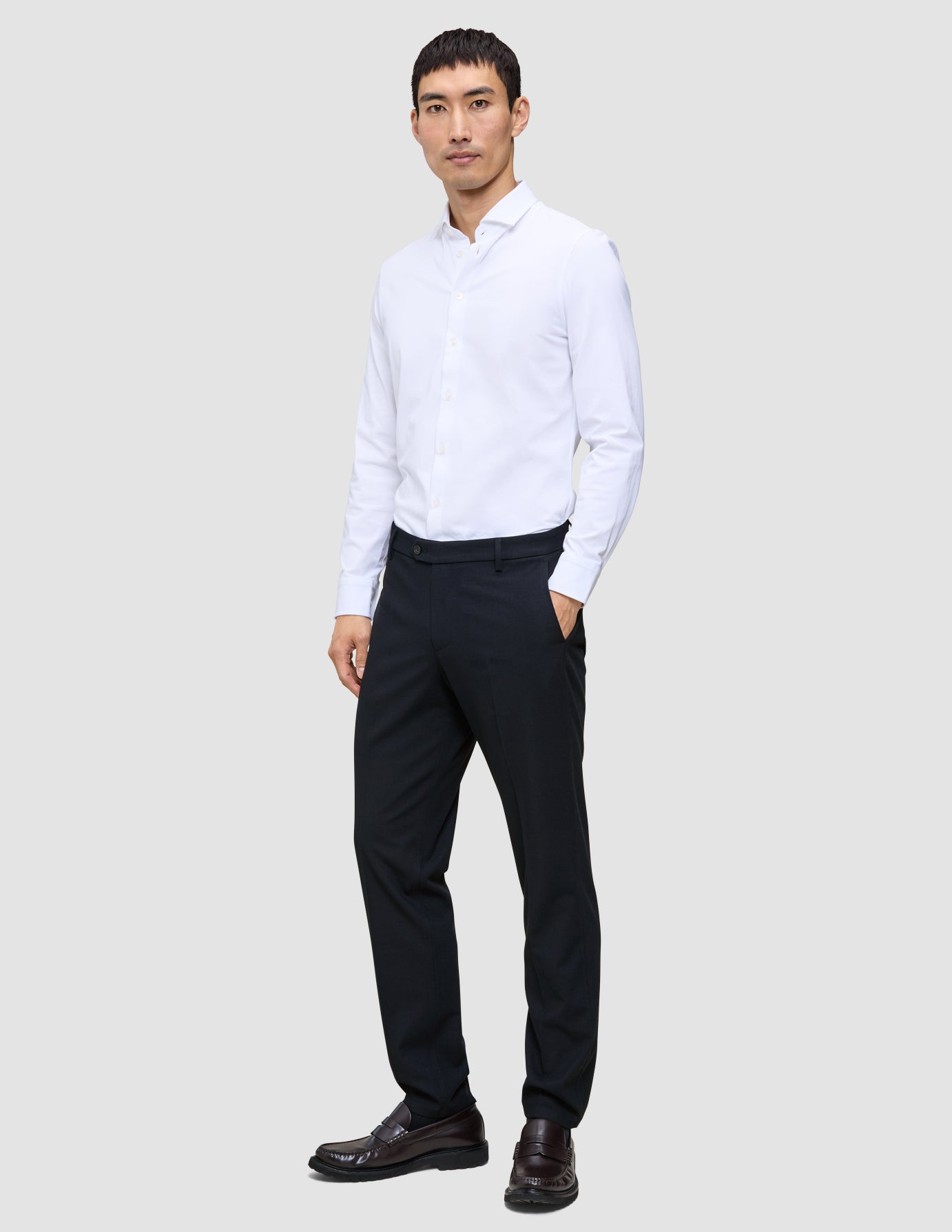 En man klädd i en vit skjorta, Motion Suit-byxor i storlek Regular i färgen Midnight Blue och mörka loafers.