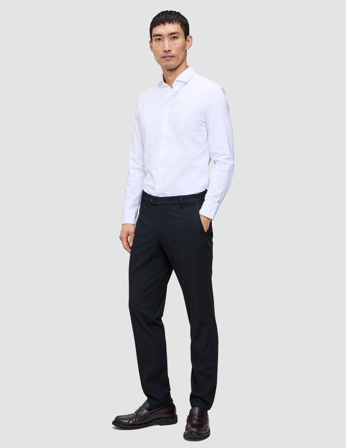 En man klädd i en vit skjorta, Motion Suit-byxor i storlek Regular i färgen Midnight Blue och mörka loafers.