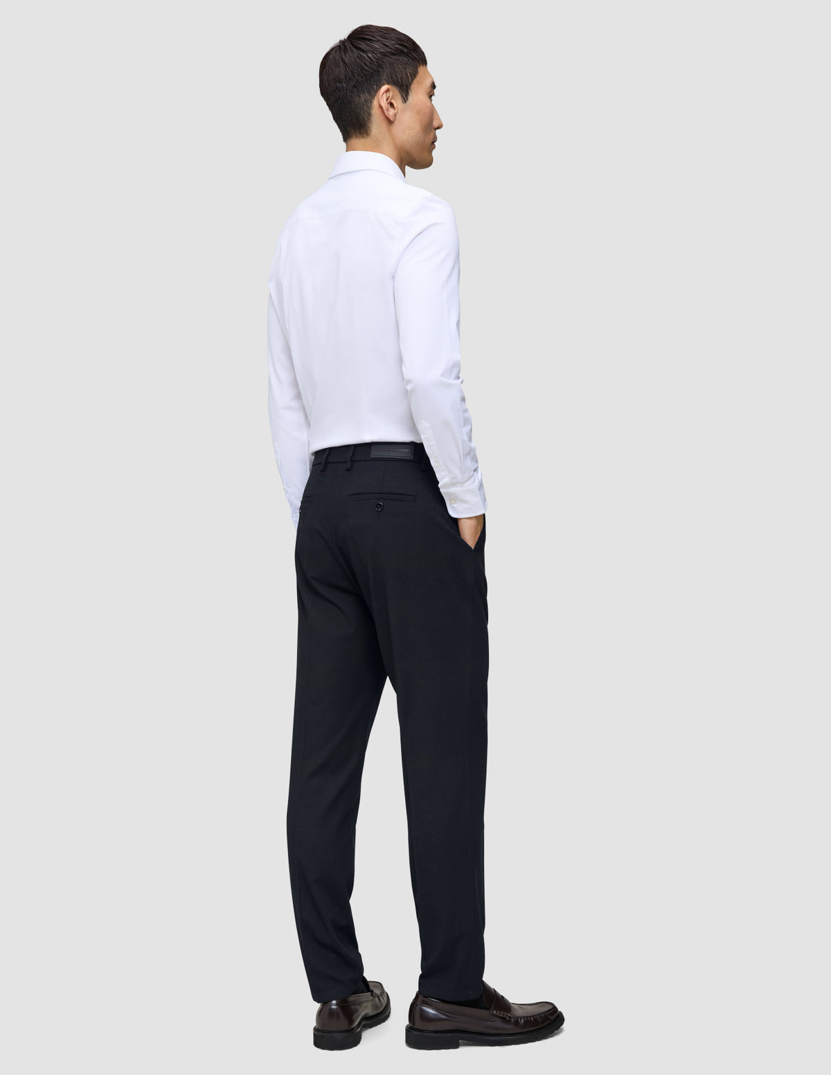 En man klädd i en vit skjorta och byxor av modellen Motion Suit Pants Regular Midnight Blue, sedd bakifrån.
