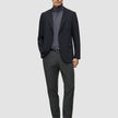 En man i svart kavaj och grå polotröja, klädd i Motion Suit Pants Regular Pepper Grey och svarta loafers.